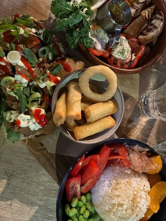 Een plank met allerlei gerechten, een pokebowl met rijst en groenten, loempia's en uienringen en kapsalon