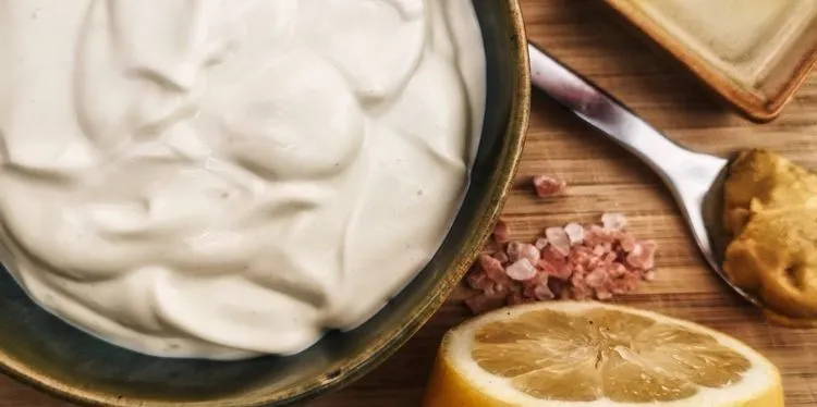 Van boven een groen bakje gevuld met een witte saus, mayonaise. Rechts hiervan zie je een citroen door de midden, himalaya zout en een lepel met mosterd.
