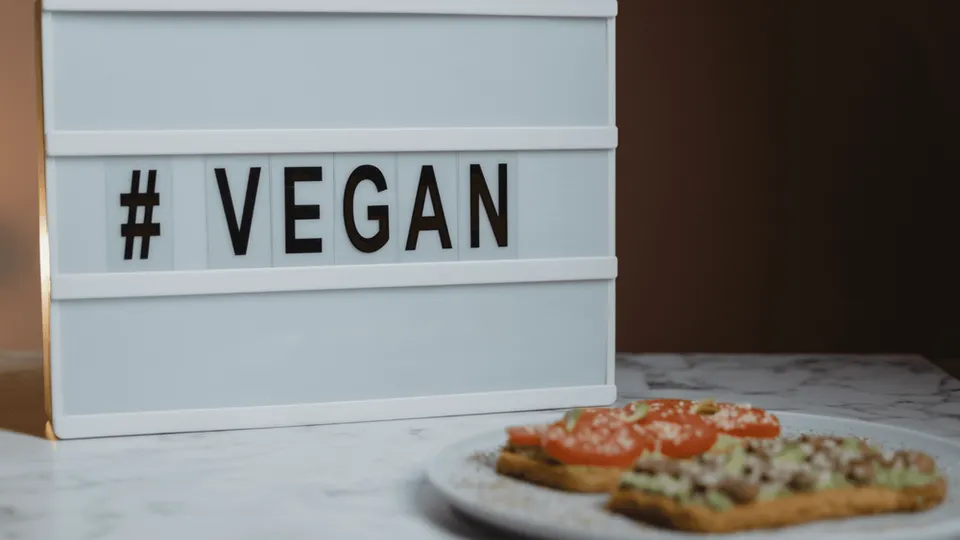 Een licht display met daarop een hashtag en het woord vegan. Ervoor liggen twee crackers met groenten